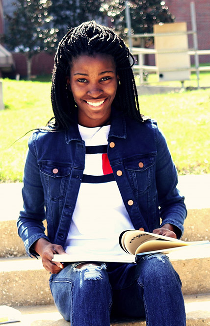 A Black student holding a book and smiling.